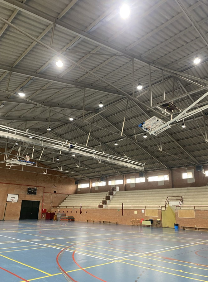 Interior de polideportivo con cubierta de fibrocemento a gran altura y estructura metálica vista