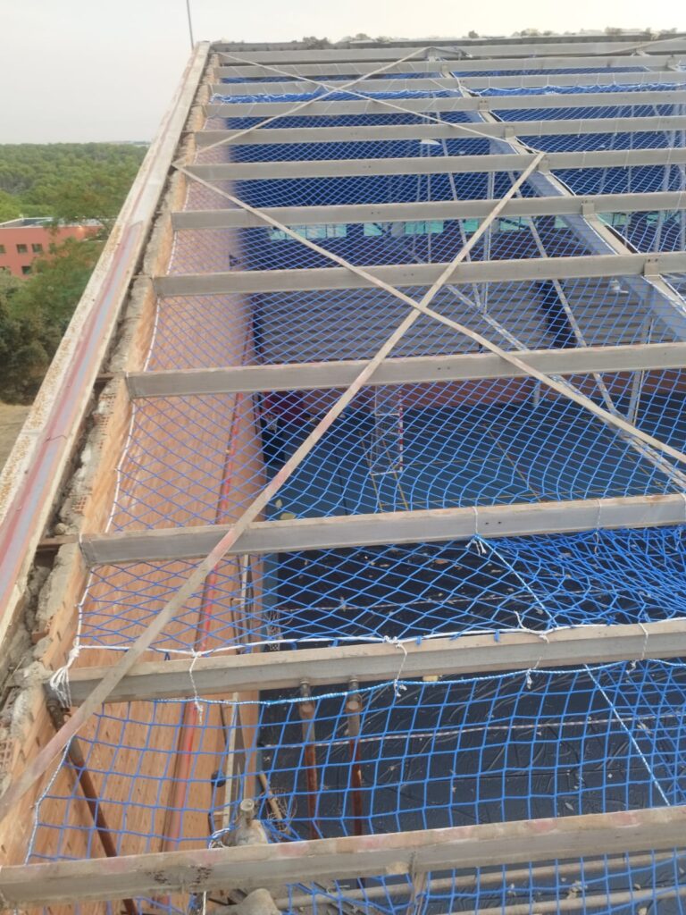 Correas de la cubierta del polideportivo del IES San Fernando tras retirar el fibrocemento, con red de seguridad y la pista protegida con plástico